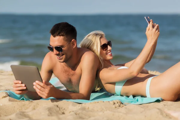 Feliz pareja con artilugios modernos acostado en la playa — Foto de Stock