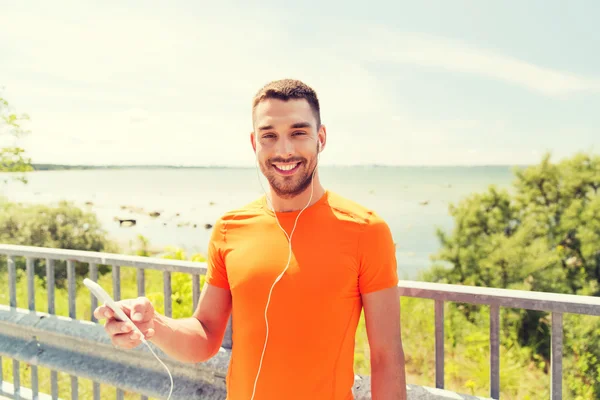 Giovane uomo sorridente con smartphone e auricolari — Foto Stock