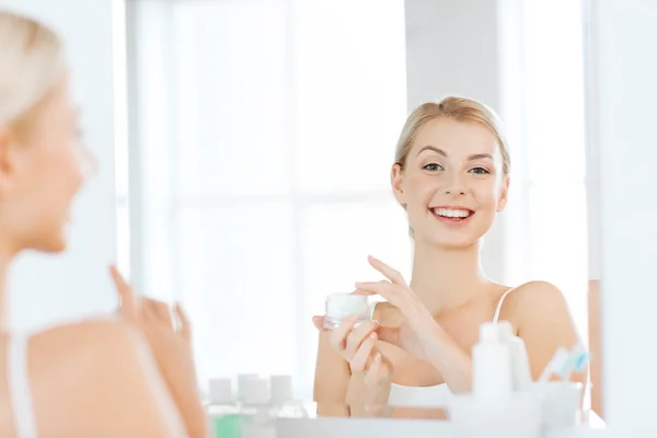 Mulher feliz aplicando creme no rosto no banheiro — Fotografia de Stock