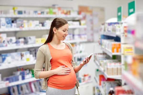 Mujer embarazada feliz con teléfono inteligente en la farmacia — Foto de Stock