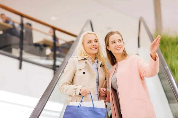 Mujeres jóvenes señalando con el dedo en la escalera mecánica en el centro comercial —  Fotos de Stock