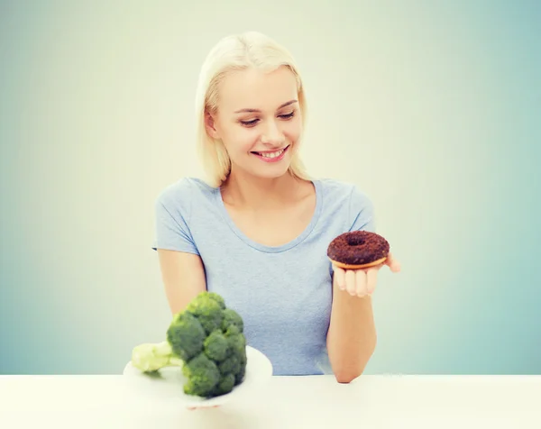 Smiling woman choosing between broccoli and donut Stock Picture