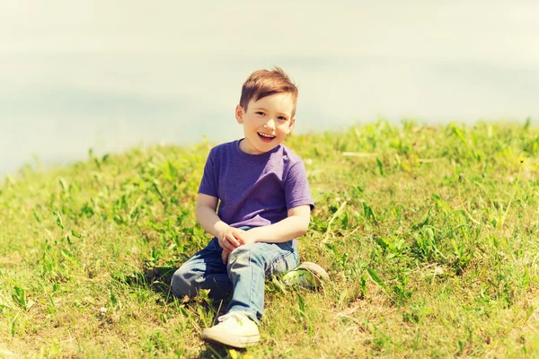 Menino feliz sentado na grama ao ar livre — Fotografia de Stock