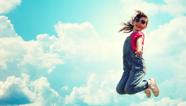 Happy little girl jumping high over blue sky — Stock fotografie