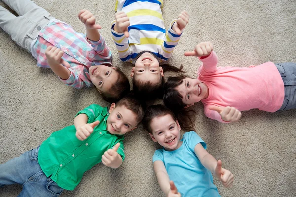 Niños felices tumbados en el suelo y mostrando los pulgares hacia arriba — Foto de Stock