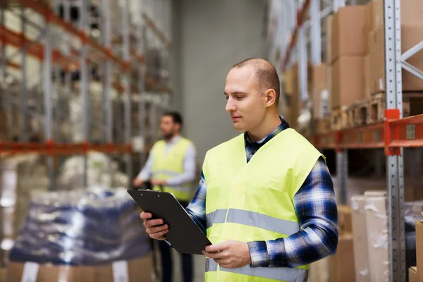 Man with clipboard in safety vest at warehouse — Stock Photo, Image