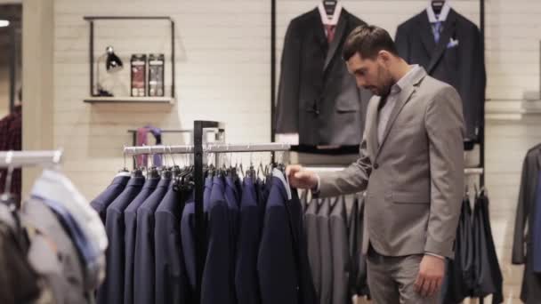 Jovem homem escolhendo terno na loja de roupas ou shopping — Vídeo de Stock