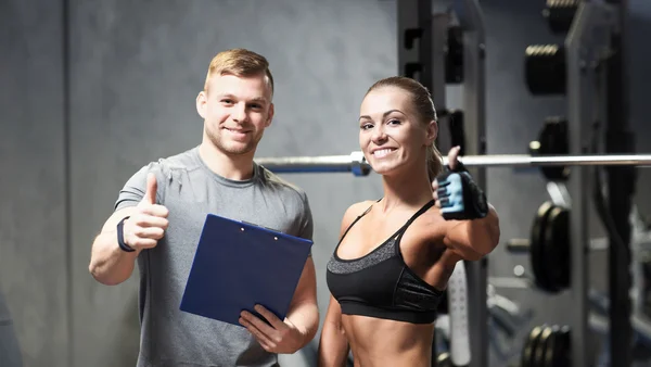 Lächelnde junge Frau mit Personal Trainer im Fitnessstudio — Stockfoto