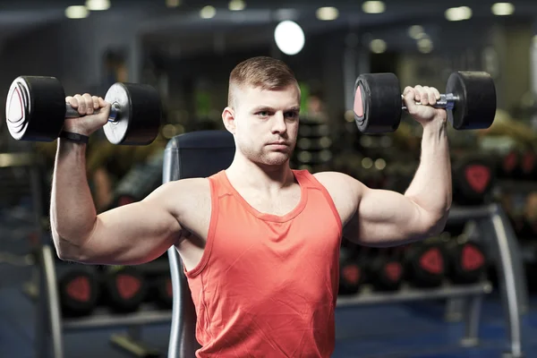 Young man with dumbbells flexing muscles in gym — Stock Photo, Image