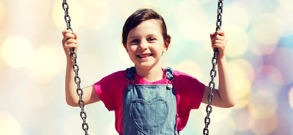 Happy little girl swinging on swing over lights — Stock Photo, Image