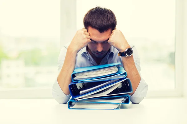 Uomo d'affari triste con pila di cartelle a ufficio — Foto Stock