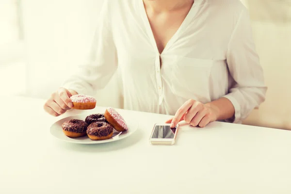 Primer plano de las manos con el teléfono inteligente y donas — Foto de Stock