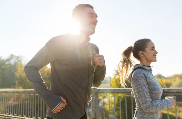 Feliz pareja con auriculares corriendo al aire libre — Foto de Stock