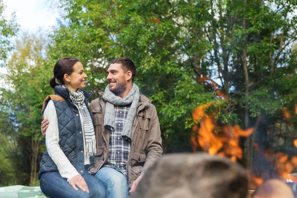 Happy couple sitting on bench near camp fire — Stock Photo, Image