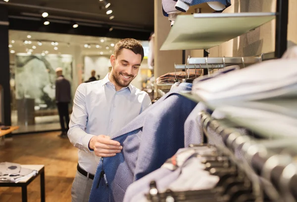 Счастливый молодой человек выбирает одежду в магазине одежды — стоковое фото
