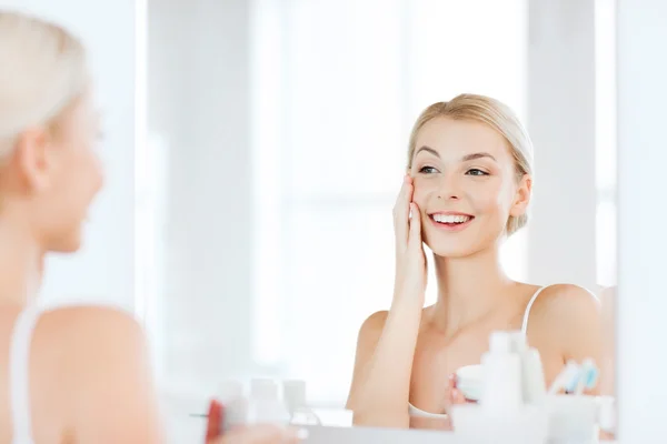 Happy woman applying cream to face at bathroom — Stock Photo, Image