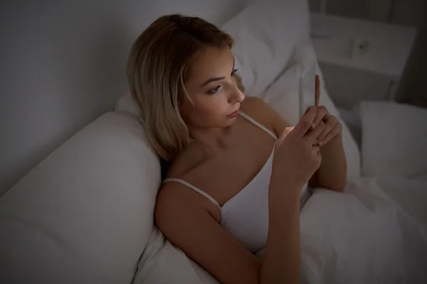 Jeune femme avec smartphone dans le lit à la maison chambre — Photo