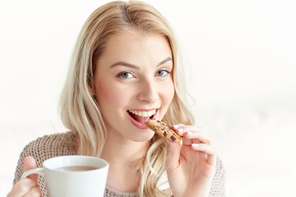 Mulher feliz com chá comer biscoito em casa — Fotografia de Stock