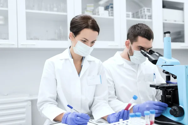 Cientistas com área de transferência e microscópio em laboratório — Fotografia de Stock