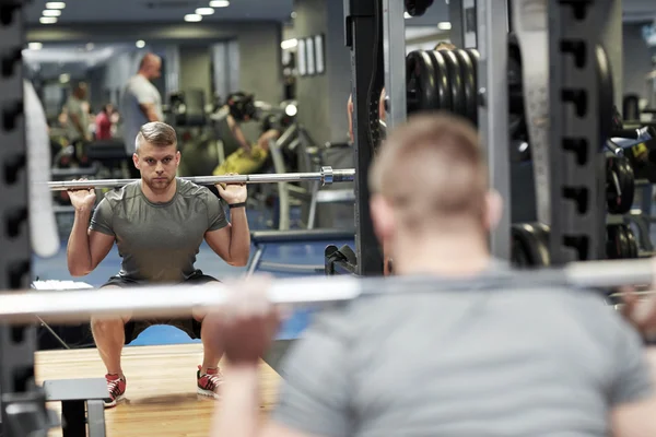 Joven hombre flexionando los músculos con barra en el gimnasio —  Fotos de Stock