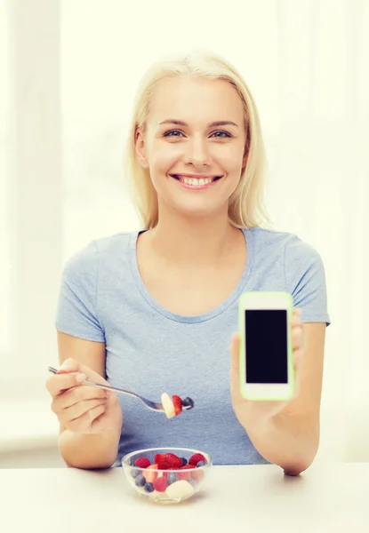 Kadın evde meyve yemek smartphone ile — Stok fotoğraf