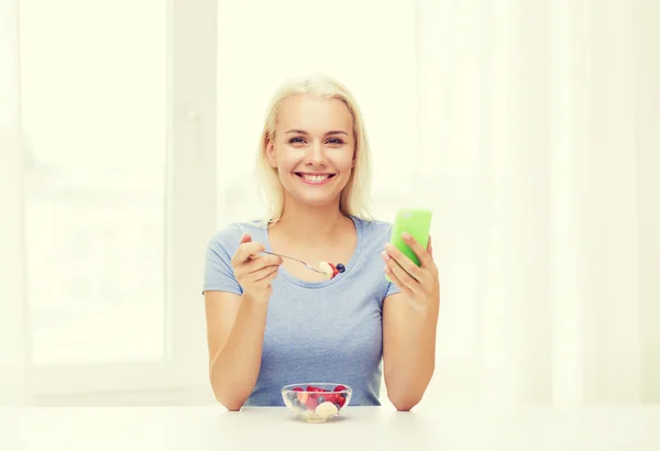 Femme avec smartphone manger des fruits à la maison — Photo