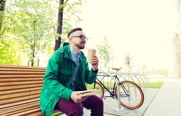 Happy hipster man eating sandwich with coffee — Stock Fotó