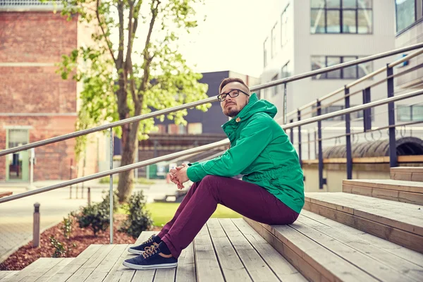 Feliz joven hipster hombre sentado en las escaleras en la ciudad —  Fotos de Stock