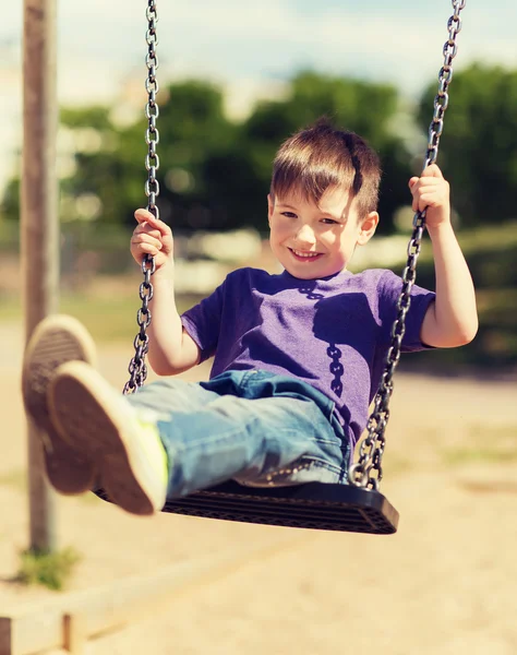 Fröhlicher kleiner Junge schaukelt auf Schaukel auf Spielplatz — Stockfoto