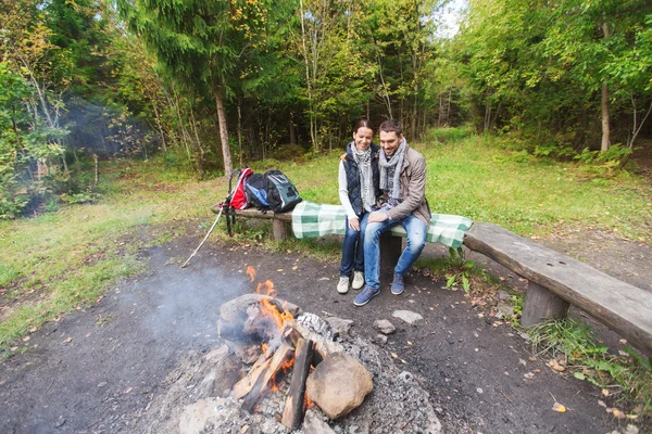Happy couple sitting on bench near camp fire — Stock Photo, Image