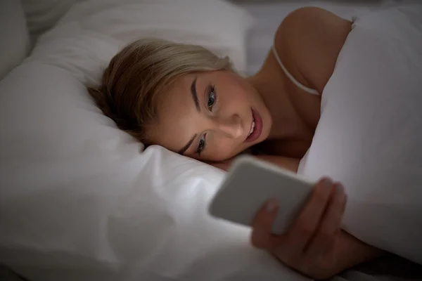 Mujer joven con teléfono inteligente en la cama en el dormitorio en casa —  Fotos de Stock