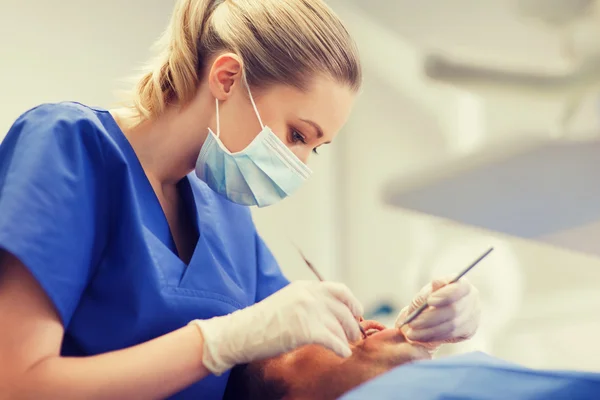 Dentista feminino verificando dentes de paciente do sexo masculino — Fotografia de Stock