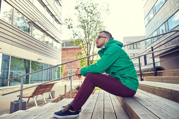 Feliz jovem hipster homem sentado em escadas na cidade — Fotografia de Stock