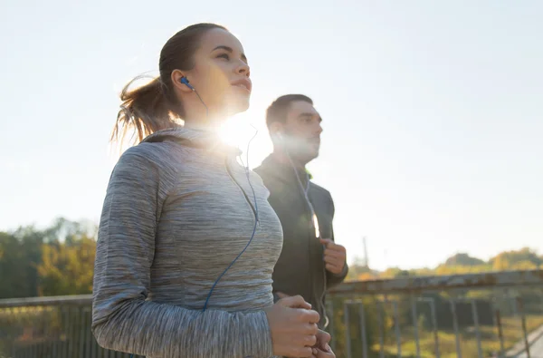 Feliz pareja con auriculares corriendo al aire libre — Foto de Stock