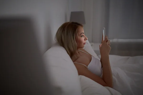 Jeune femme avec smartphone dans le lit à la maison chambre — Photo