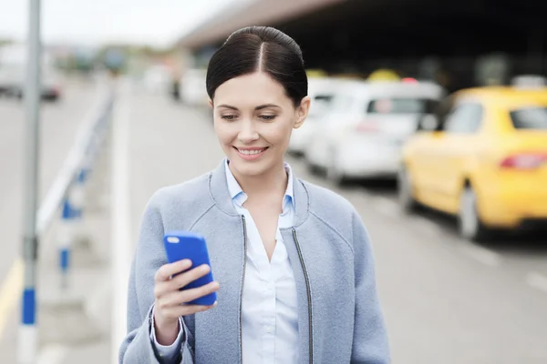 Lachende vrouw met smartphone over taxi in stad — Stockfoto