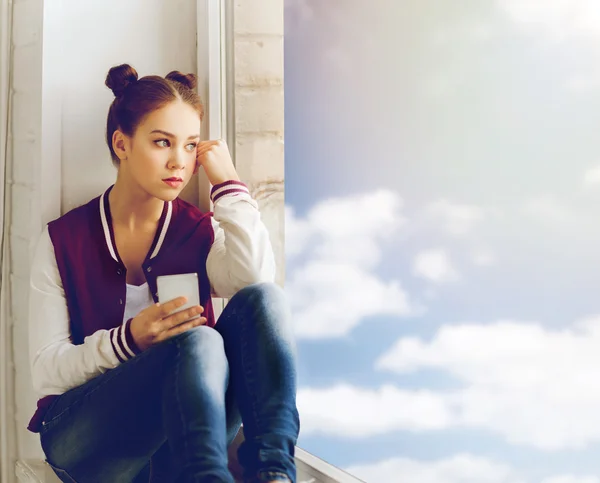 Tonårig flicka sitter på fönsterkarmen med smartphone — Stockfoto