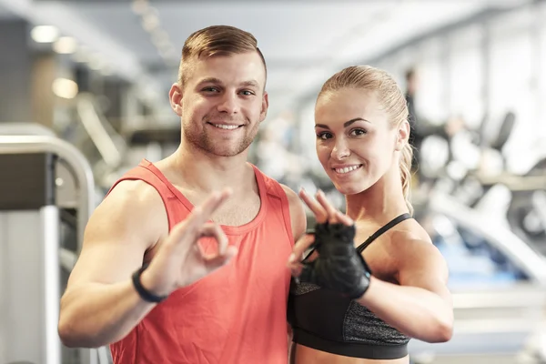 Sonriente hombre y mujer mostrando ok signo de mano en el gimnasio —  Fotos de Stock