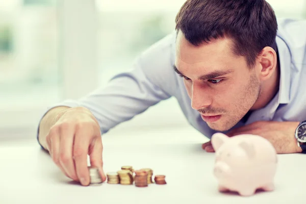 Affärsman med spargris och mynt på kontor — Stockfoto