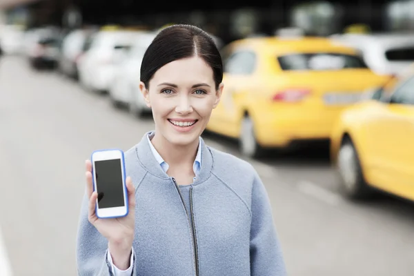 Lachende vrouw met smartphone over taxi in stad — Stockfoto