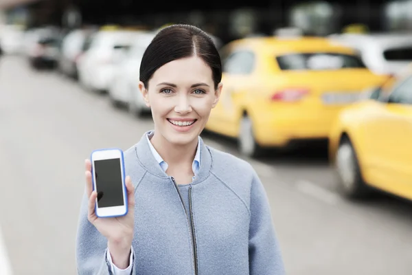 Smiling woman showing smartphone over taxi in city — Stock Photo, Image