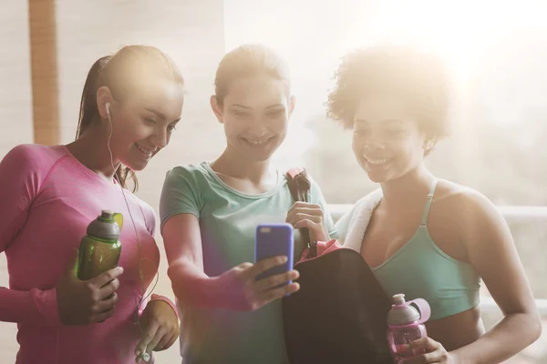 Happy women with bottles and smartphone in gym — Stock Photo, Image