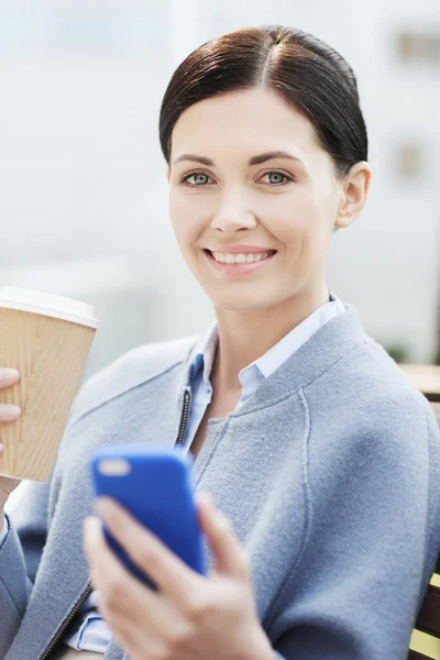 Улыбающаяся женщина с кофе и смартфоном — стоковое фото
