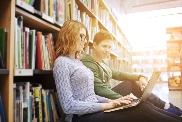 Zadowoleni uczniowie z laptopa w bibliotece — Zdjęcie stockowe