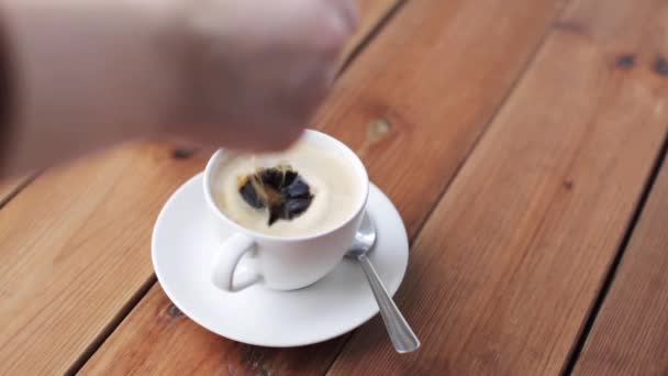 Main laissant tomber le sucre dans une tasse à café sur la table — Video