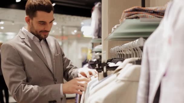 Giovane uomo che sceglie vestiti in negozio di abbigliamento — Video Stock