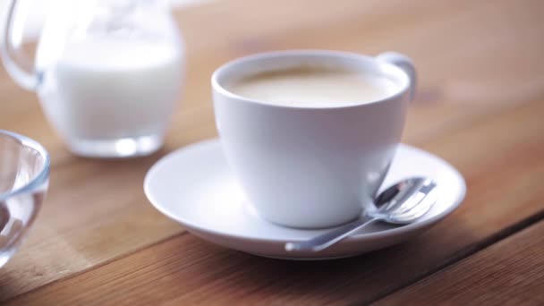 Taza de café y frijoles vertiendo a la mesa de madera — Vídeos de Stock