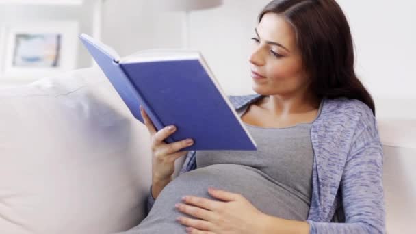 Счастливая беременная женщина читает книгу дома — стоковое видео