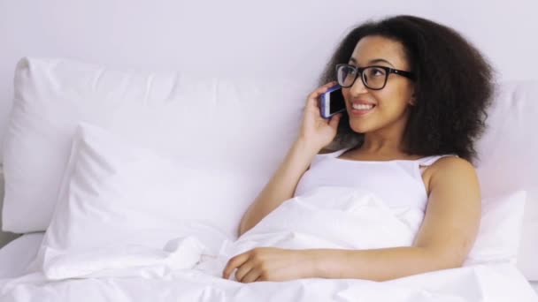 African woman calling on smartphone in bed at home — Stock Video