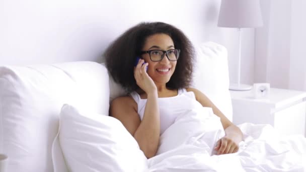 African woman calling on smartphone in bed at home — Stock Video